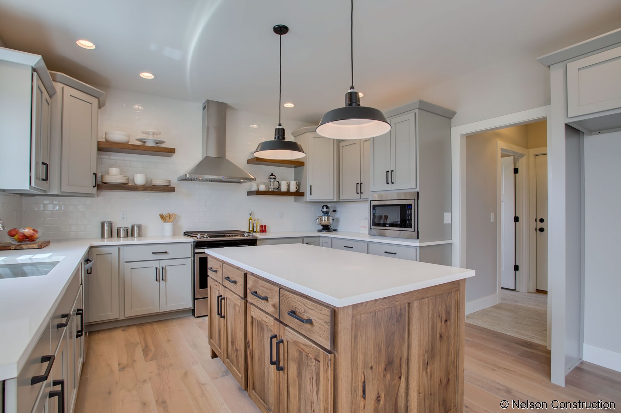 The designer inspired kitchen of this new home features floating shelves, subway tile backsplash, and a stainless hood.