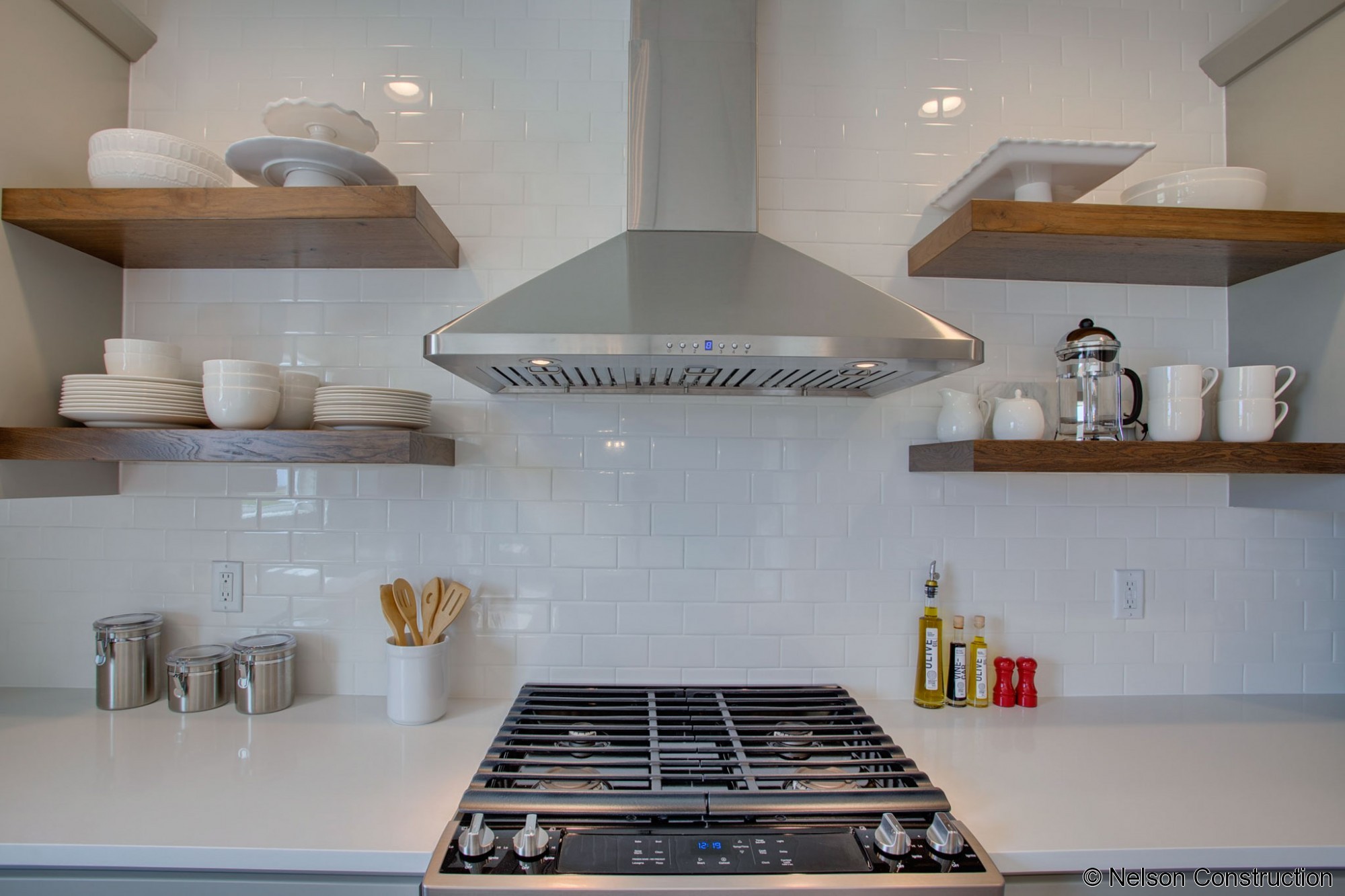 The designer inspired kitchen of this new home features floating shelves, subway tile backsplash, and a stainless hood.